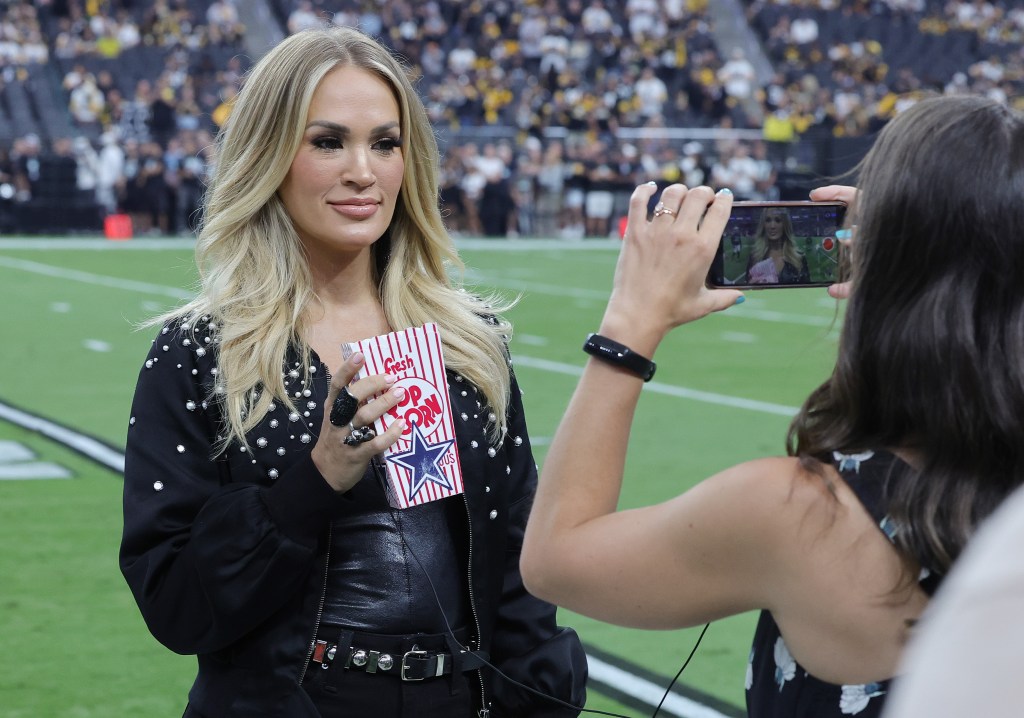 Recording artist Carrie Underwood films a promo on a football field, holding a "Fresh Popcorn" box with a Dallas Cowboys star.