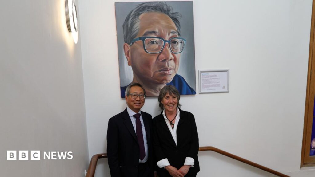 Mr Gerald Gui and artist and former patient Ruth Swain smiling for a photo under his portrait at the Royal Marsden Hospital. They are in the staircase.
