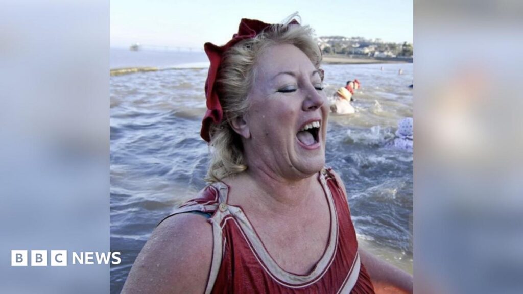 Linda Strong in Clevedon Marine Lake. Her expression and body language show the water is cold, but she is smiling nonetheless. Clevedon Pier can be seen behind.