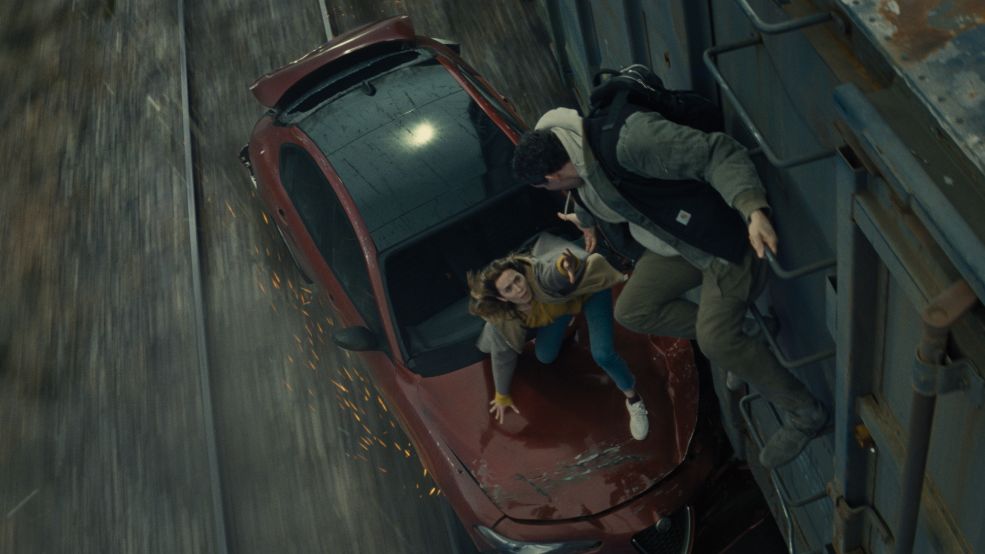 A man and a woman attempting to board a train from their stricken car that is being dragged along the track.